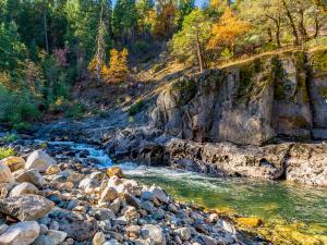 california stream in the sunlight beneath a rocky cliff and fall foliage